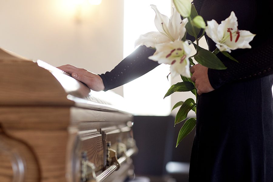 Funeral Home Insurance - Closeup of Woman With Flowers Placing a Hand on a Casket