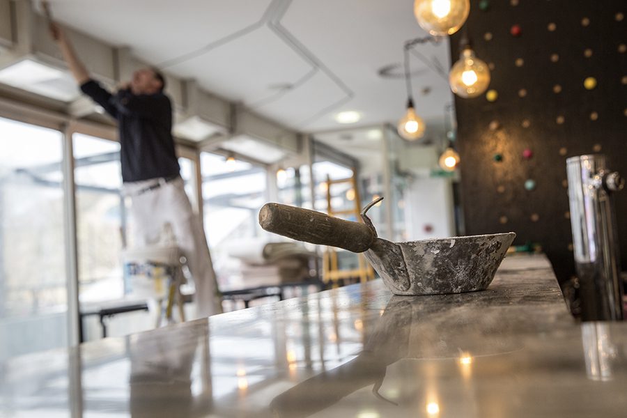 Restoration Contractor Insurance - View of a Construction Worker Fixing and Repairing a Ceiling in a Restaurant With Tools and on a Ladder in the Background and Blurred