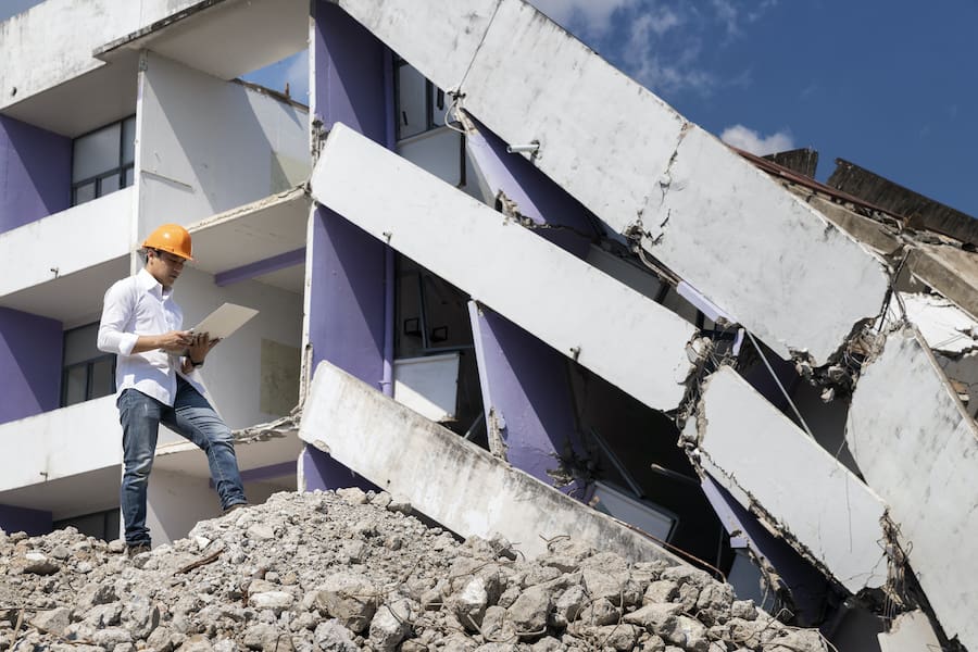 Commercial-Earthquake-Insurance-Engineer holding laptop is checking for destruction, demolishing building.